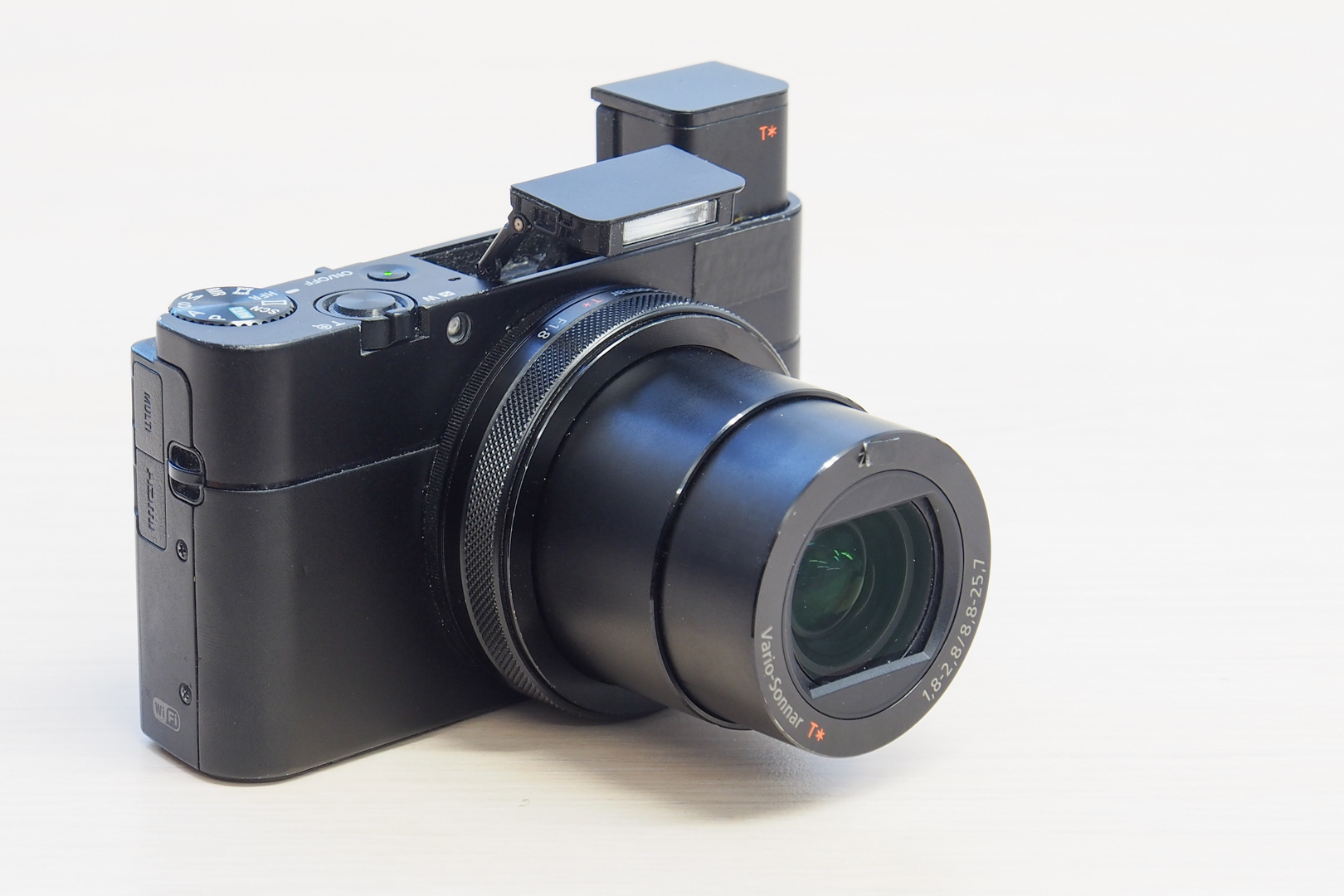 Kompaktni fotoaparat crne boje sa izvučenim objektivom, bljeskalicom i digitalnim tražilom.